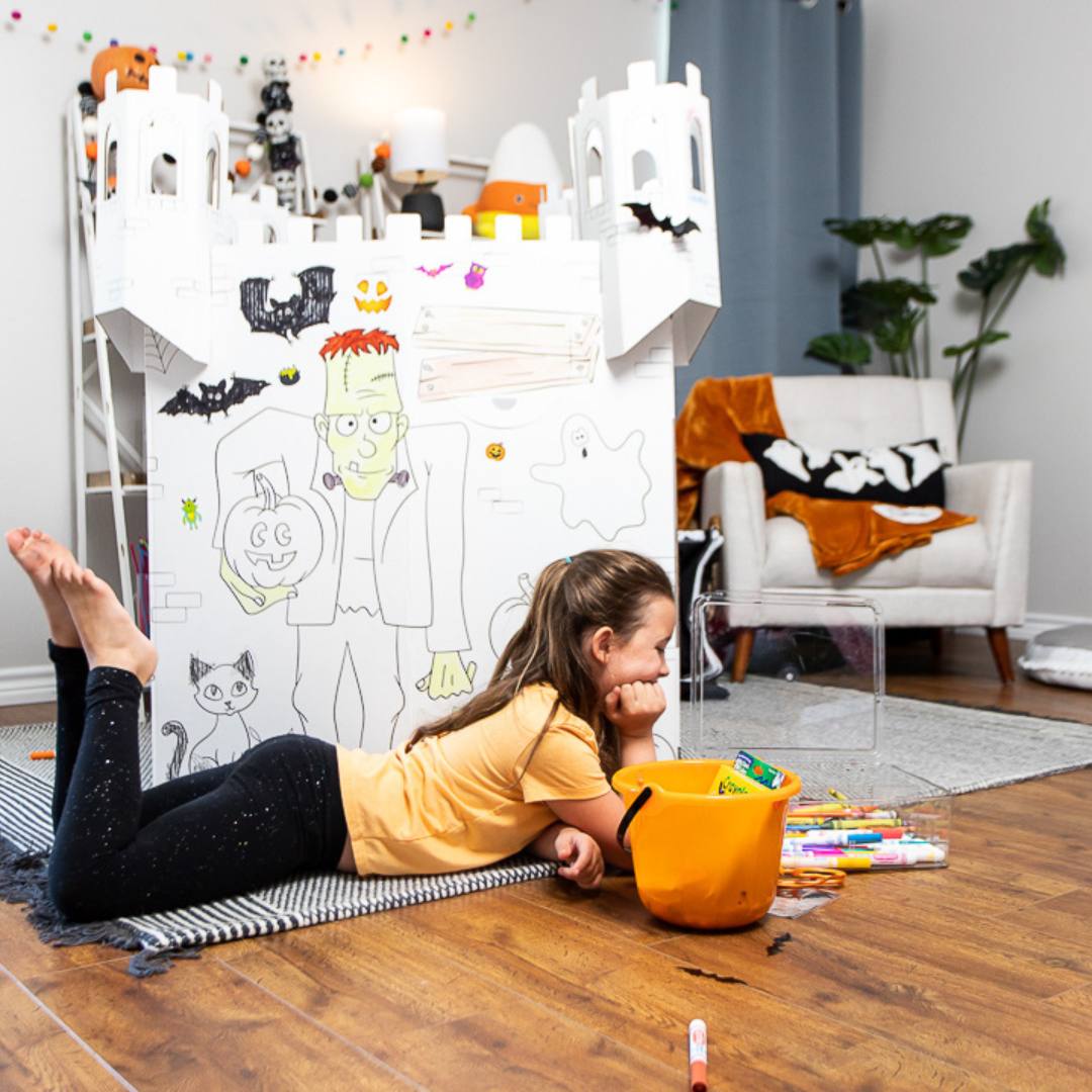 Playboxes Halloween haunted house castle image showing a girl laying outside the Halloween haunted house castle playhouse looking at the markers and choosing which one to color with