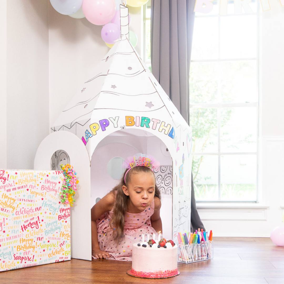 Playboxes birthday cupcake image showing girl sitting in birthday cupcake playhouse with candle on top and a birthday cake in front of her blowing out the candles on the cake