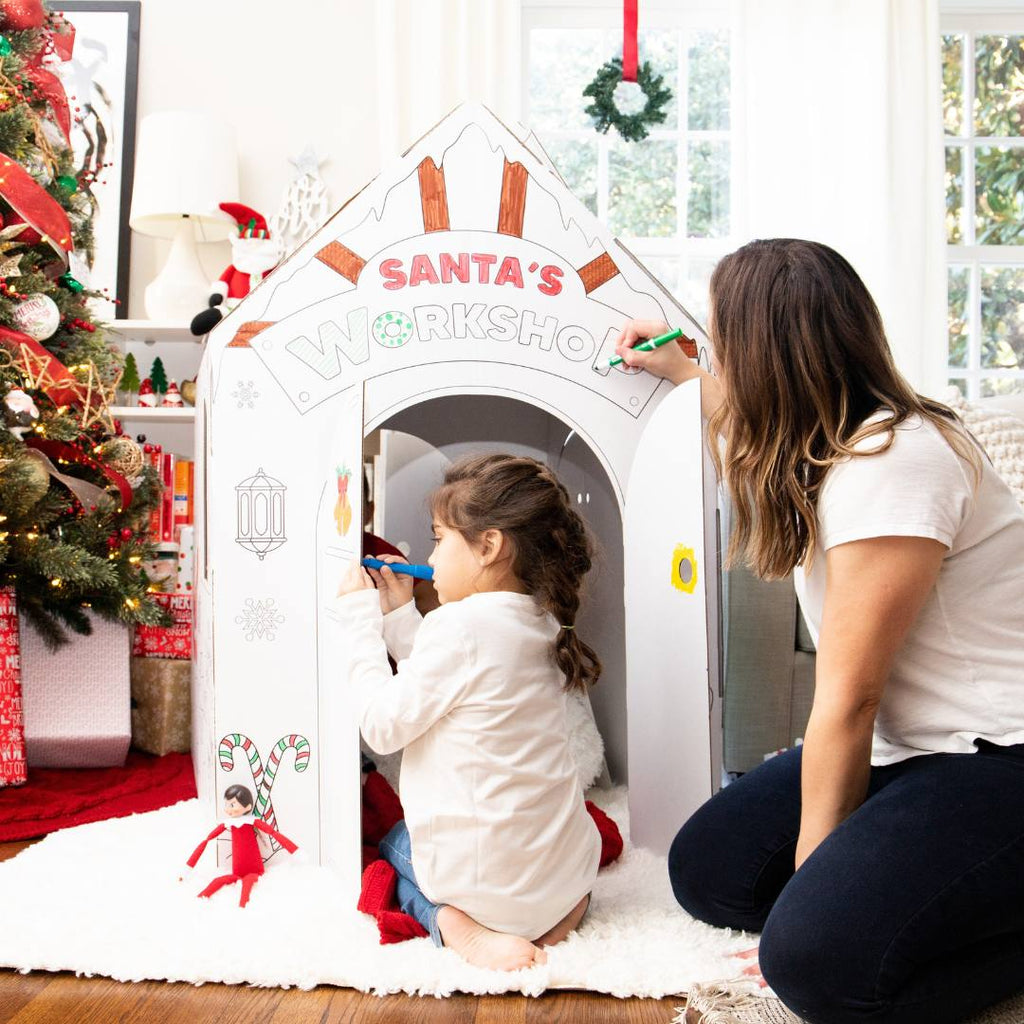Playboxes Santa’s Workshop playhouse image showing woman and little girl sitting outside the Santa’s Workshop Christmas playhouse coloring the images printed on the the outside of the box