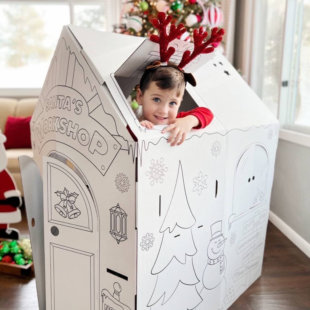 Playboxes Santa’s Workshop playhouse image showing a boy standing inside the Santa’s Workshop Christmas playhouse poking his head out of the cutout on top of the box smiling wearing reindeer antlers on his head